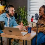 Dois podcasters gravando um episódio em estúdio com microfones e fones de ouvido.