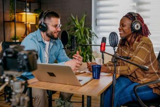 Dois podcasters gravando um episódio em estúdio com microfones e fones de ouvido.
