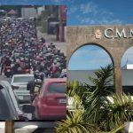Engarrafamento com motos e carros em frente à CMM, com céu azul e vegetação.