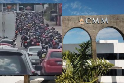 Engarrafamento com motos e carros em frente à CMM, com céu azul e vegetação.