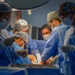 Equipe médica realiza cirurgia em centro cirúrgico com luzes intensas.