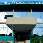 Fachada da Prefeitura Municipal de Manaus, com céu azul refletido nos vidros.