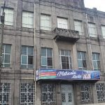 Fachada de escola cinza com letreiro de matrículas abertas.