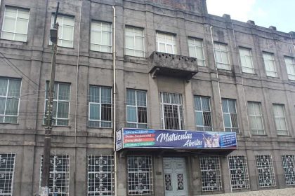 Fachada de escola cinza com letreiro de matrículas abertas.