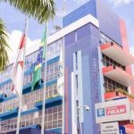 Fachada do prédio da FIEMG com bandeiras do Brasil e de estados, com palmeiras e céu azul ao fundo.