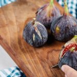 Figos frescos em uma tábua de madeira com uma faca cortando um deles.