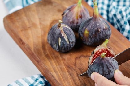 Figos frescos em uma tábua de madeira com uma faca cortando um deles.