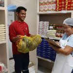 Funcionário entrega abóboras para uma mulher que verifica estoque em mercearia.