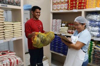 Funcionário entrega abóboras para uma mulher que verifica estoque em mercearia.