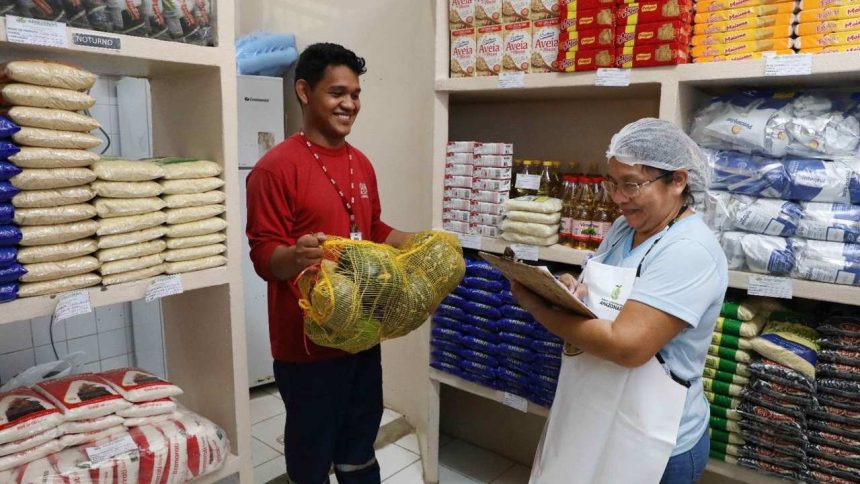 Funcionário entrega abóboras para uma mulher que verifica estoque em mercearia.