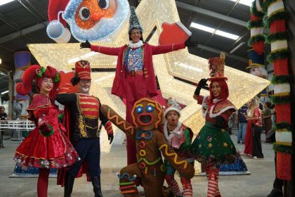 Grupo de artistas fantasiados em cenário natalino, com destaque para a decoração e iluminação.