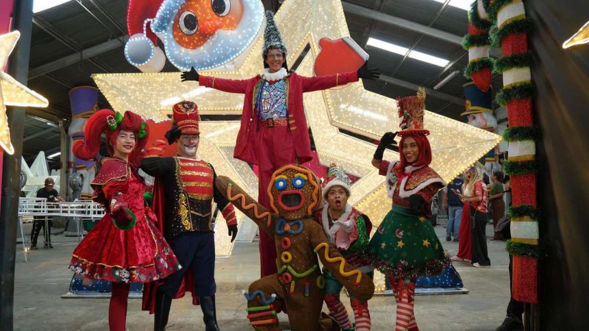 Grupo de artistas fantasiados em cenário natalino, com destaque para a decoração e iluminação.