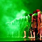 Grupo de bailarinos em um palco com iluminação verde, parte da programação do II Arte Ocupa no Teatro ICBEU.