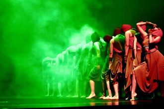 Grupo de bailarinos em um palco com iluminação verde, parte da programação do II Arte Ocupa no Teatro ICBEU.