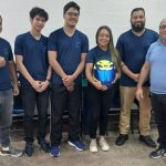 Grupo de estudantes vestindo uniformes da Fucapi, segurando um capacete, em ambiente interno.