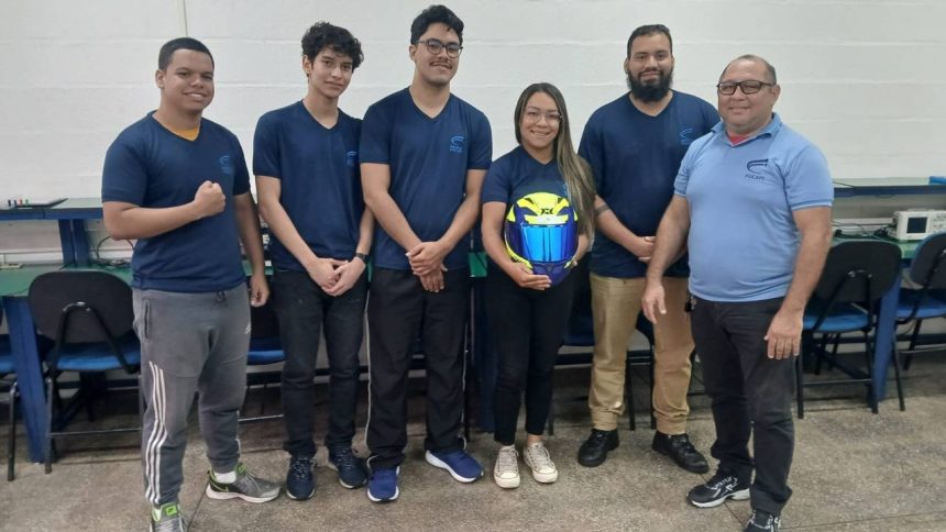 Grupo de estudantes vestindo uniformes da Fucapi, segurando um capacete, em ambiente interno.