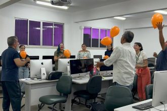 Grupo em oficina sobre cinema, educação e direitos humanos, com balões laranja em um ambiente de computadores.