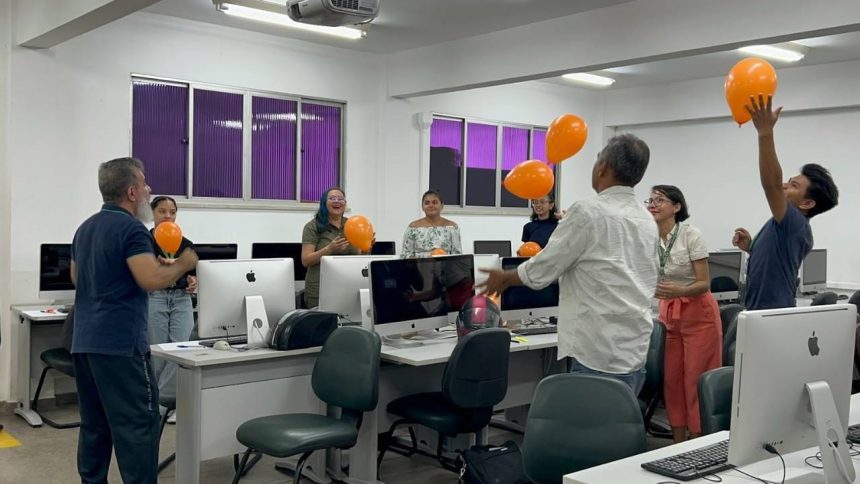 Grupo em oficina sobre cinema, educação e direitos humanos, com balões laranja em um ambiente de computadores.