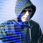 Hacker com máscara e capuz segurando smartphone com cadeado digital, em um fundo de código binário.