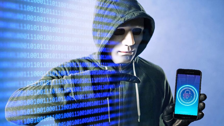 Hacker com máscara e capuz segurando smartphone com cadeado digital, em um fundo de código binário.