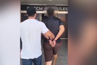 Homem algemado sendo conduzido por policial após prisão em Manaus.