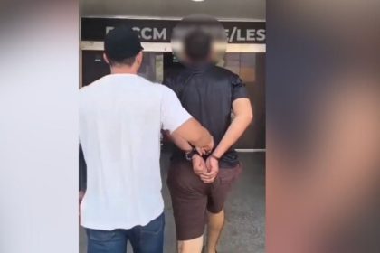 Homem algemado sendo conduzido por policial após prisão em Manaus.
