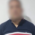 Homem com camisa azul e detalhes em branco e vermelho, rosto desfocado.