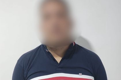 Homem com camisa azul e detalhes em branco e vermelho, rosto desfocado.