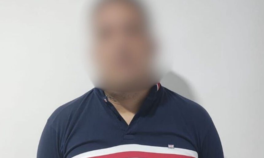 Homem com camisa azul e detalhes em branco e vermelho, rosto desfocado.