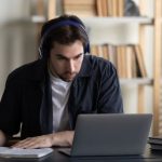 Homem com fones de ouvido estudando online em frente ao laptop