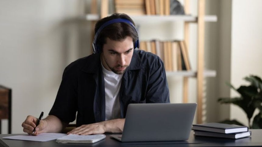 Homem com fones de ouvido estudando online em frente ao laptop