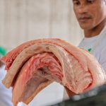 Homem segura grandes pedaços de pirarucu, peixe de água doce.