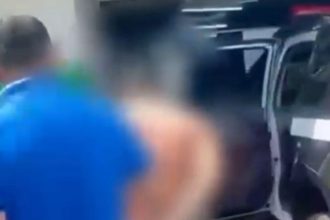 Homem sendo preso perto de um carro, possivelmente após agressão.