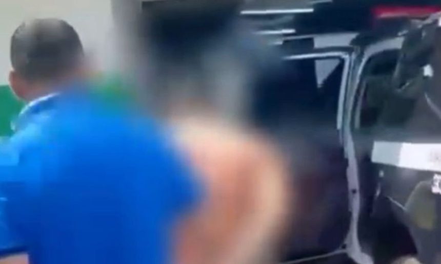 Homem sendo preso perto de um carro, possivelmente após agressão.