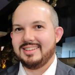 Homem sorrindo com barba, possivelmente em evento de inovação