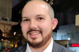 Homem sorrindo com barba, possivelmente em evento de inovação