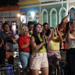 Público aplaude evento de samba ao ar livre, com pessoas de todas as idades.