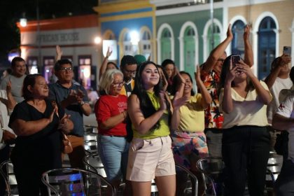 Público aplaude evento de samba ao ar livre, com pessoas de todas as idades.