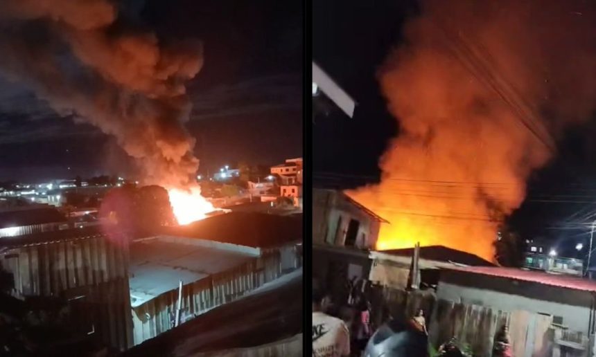 Incêndio destrói casa à noite, com fumaça e chamas intensas.