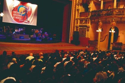 Interior de teatro com palco e plateia lotada durante o Festival Amazonas de Música.
