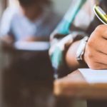 Mão escrevendo em prova, caneta dourada em foco