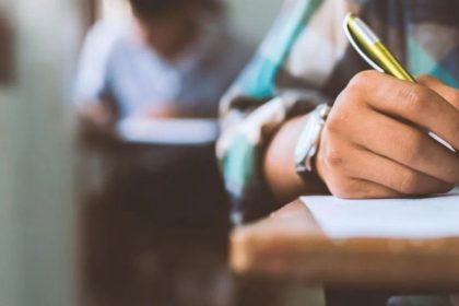 Mão escrevendo em prova, caneta dourada em foco