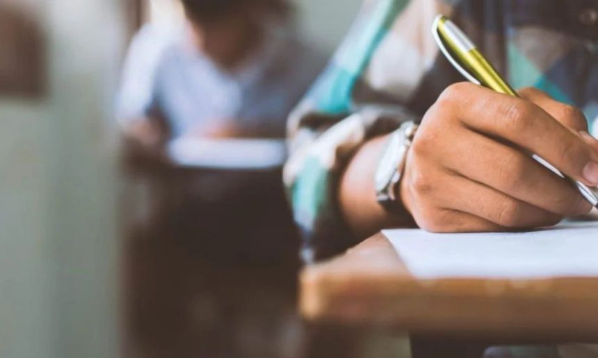 Mão escrevendo em prova, caneta dourada em foco