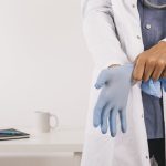 Médico vestindo luva cirúrgica azul. Visão em close, com estetoscópio.