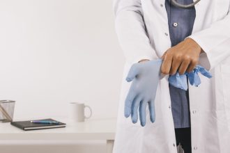 Médico vestindo luva cirúrgica azul. Visão em close, com estetoscópio.