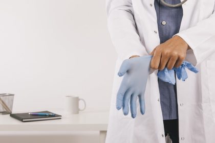 Médico vestindo luva cirúrgica azul. Visão em close, com estetoscópio.