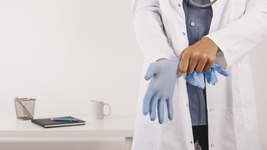 Médico vestindo luva cirúrgica azul. Visão em close, com estetoscópio.