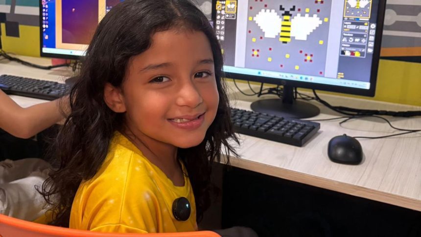Menina sorrindo em curso de criação de games com um computador mostrando um desenho de abelha em pixels.