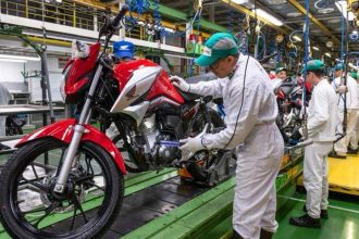Montagem de motocicleta Honda em fábrica, com operário inspecionando o veículo na linha de produção.