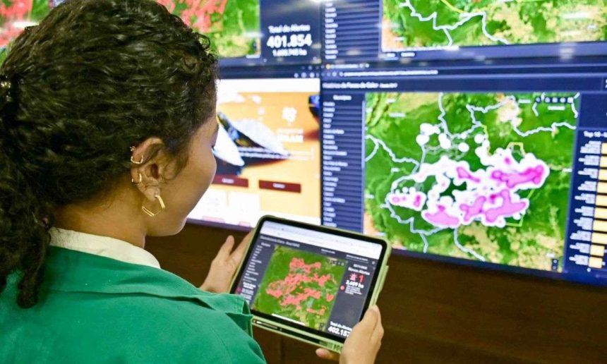 Mulher analisa dados de focos de calor em tablet, com mapas e painéis de dados ao fundo.